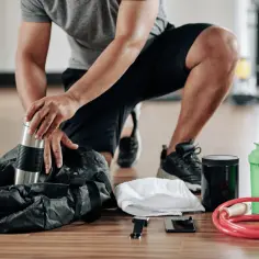 Pakowanie torby na siłownię: bidon, odżywka, ręcznik, telefon, smartwatch i skakanka.