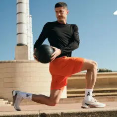 Robert Lewandowski w pomarańczowych spodenkach i czarnej bluzie wykonuje ćwiczenie z piłką. Idealne jakie buty do crossfitu zapewniają stabilność.