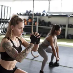 Dwie kobiety wykonują przysiady z kettlebell. To przykład treningu funkcjonalnego, co to za ćwiczenia?