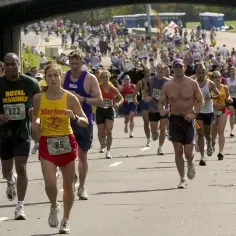 Uczestnicy maratonu biegną pod mostem, jeden z nich ma na koszulce napis "Marines".