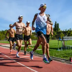 Biegacze na bieżni stadionu, która ma 400 metrów. Słońce świeci, a zawodnicy w skupieniu pokonują kolejne metry.