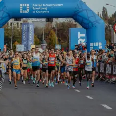 Biegacze przekraczają niebieską bramę startową maratonu w Krakowie. Zastanawiasz się, ile trwa maraton? Ci zawodnicy dopiero zaczynają swoją drogę.