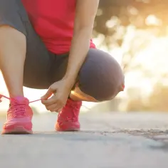 Kobieta w różowych butach sportowych zawiązuje sznurówki. Szybki marsz to świetny sposób na poprawę kondycji i samopoczucia.