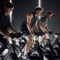 Trzy osoby ćwiczą na rowerach stacjonarnych. To świetny sposób na trening, czyli indoor cycling.