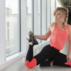 Kobieta w sportowym stroju wykonuje ćwiczenia rozciągające, co jest idealnym przykładem na fitness w domu.