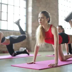 Kobiety ćwiczą pilates, co daje im siłę i elastyczność. W tle duże okna i ceglana ściana.