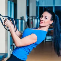 Kobieta wykonuje ćwiczenia na TRX, napinając mięśnie.