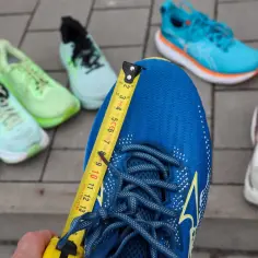 Miarka mierzy niebieski but do biegania. Czy buty do biegania powinny być większe? W tle inne kolorowe buty.