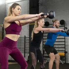 Trzy osoby wykonują trening obwodowy z kettlebellami. To świetny sposób na budowanie siły i wytrzymałości.