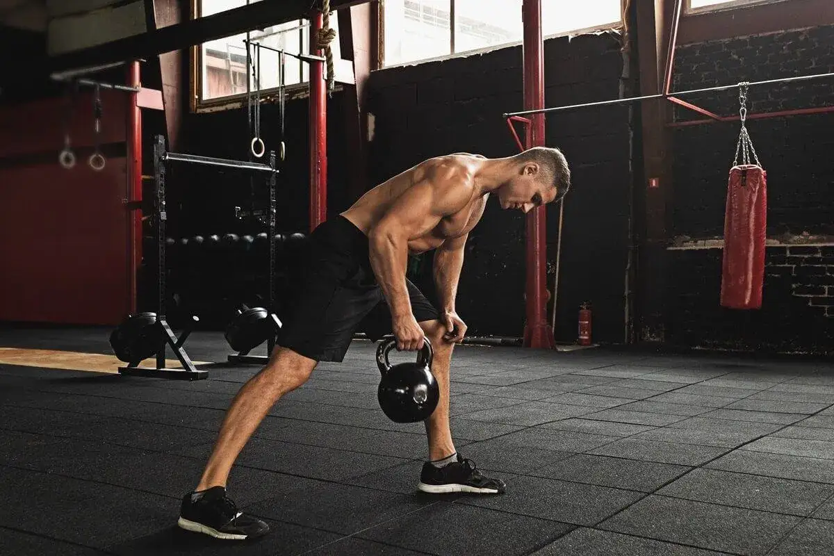 Mężczyzna wykonuje ćwiczenie z kettlebell. To przykład treningu funkcjonalnego, który poprawia siłę i koordynację.
