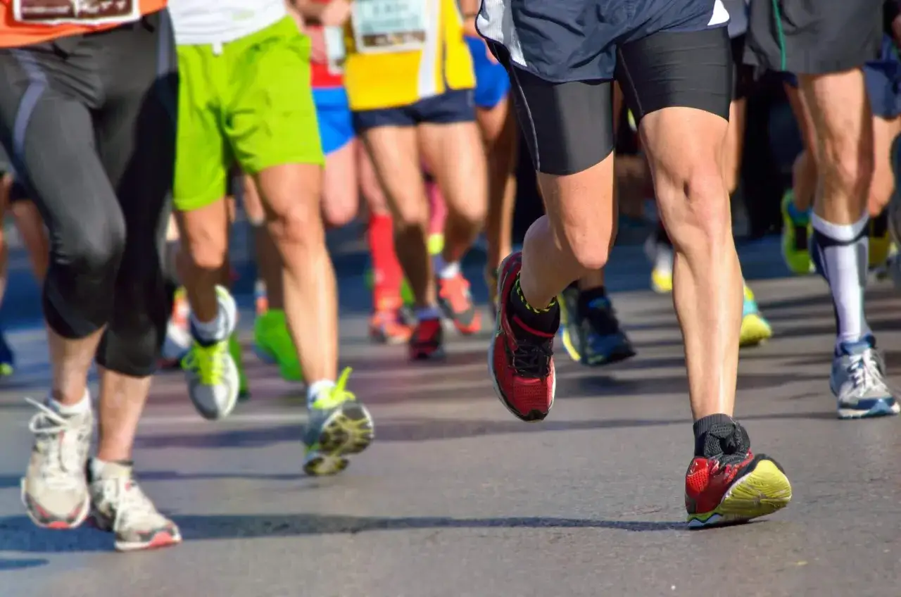 Biegacze w kolorowych strojach na trasie, przygotowujący się do półmaratonu. Skupienie na nogach i butach, symbolizujące determinację i wysiłek.
