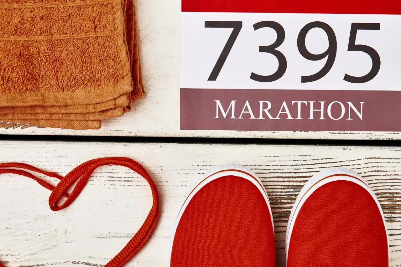 Pomarańczowy ręcznik, sznurówki ułożone w serce i czerwone trampki. Obok numer 7395 i napis MARATHON. Czy to odpowiedź na pytanie, ile trwa maraton?