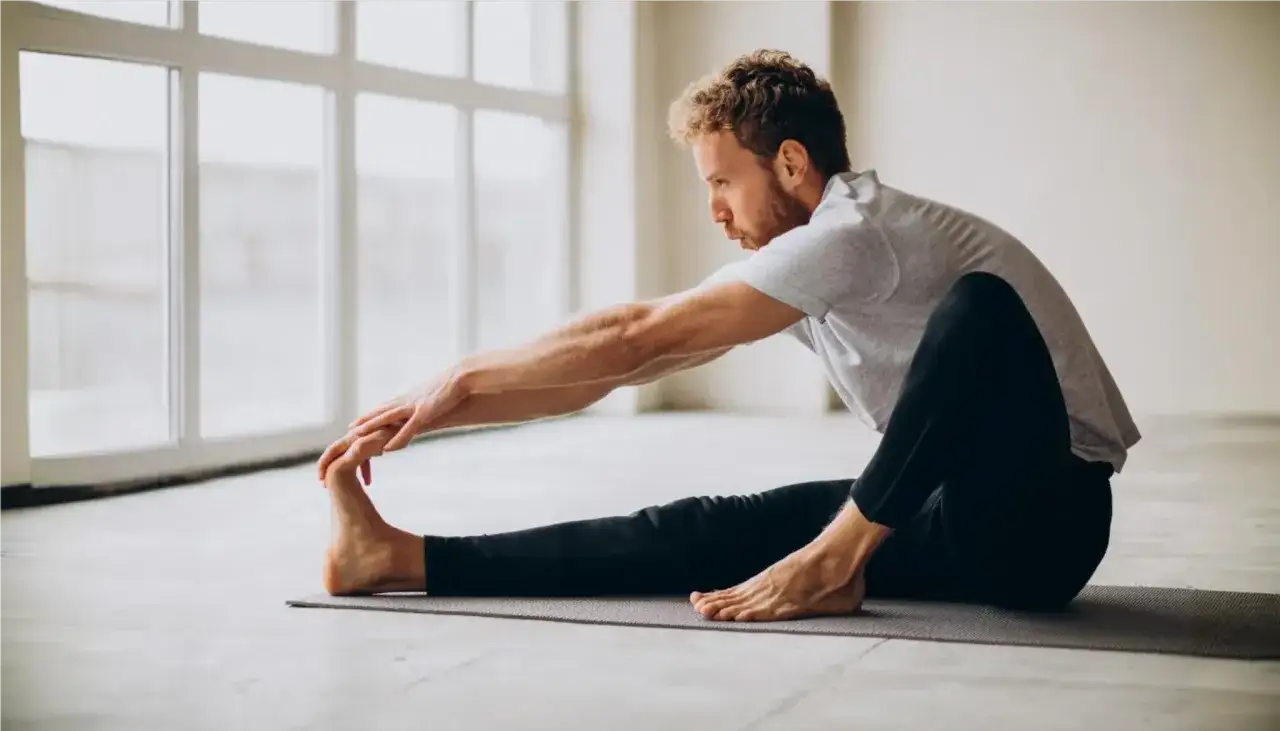 Mężczyzna ćwiczy pilates, rozciągając nogę. Widzisz, co daje pilates: elastyczność i siłę.