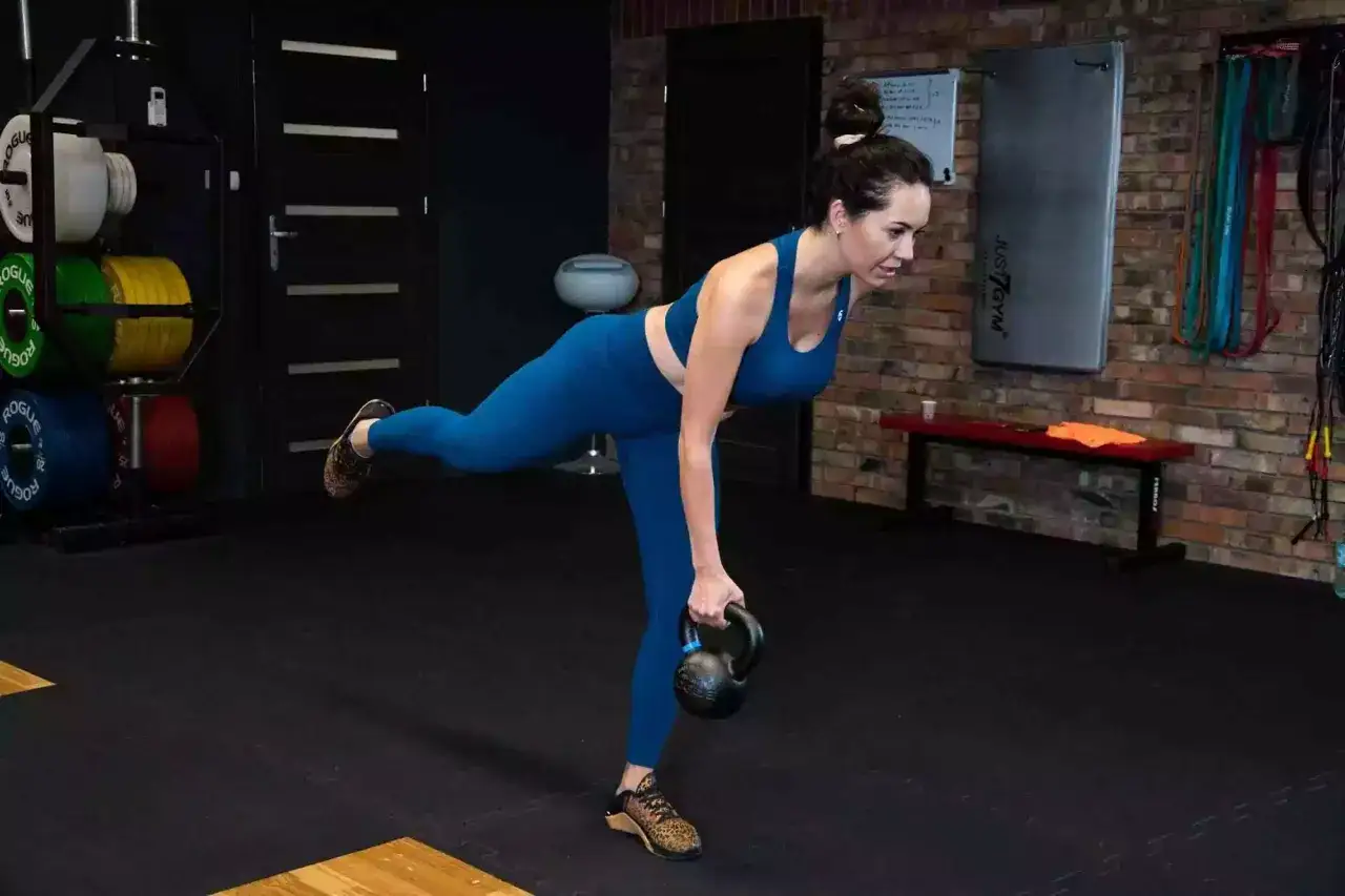 Kobieta wykonuje martwy ciąg na jednej nodze z kettlebell, ćwicząc dolne partie ciała.